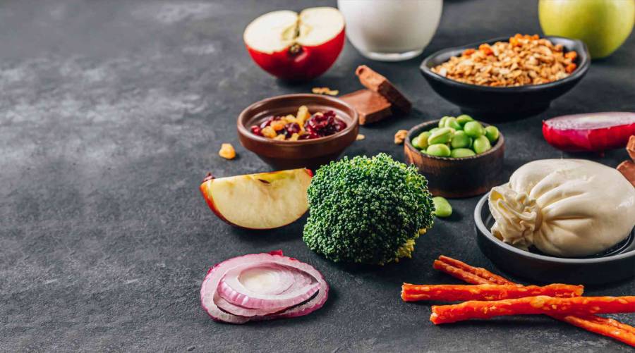 Assorted high-FODMAP foods including apples, onions, wheat, dairy products, beans, and artificial sweeteners on a wooden table.