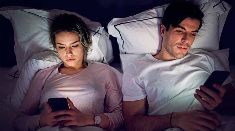 Young couple using phone in bed at night affecting sleep patterns