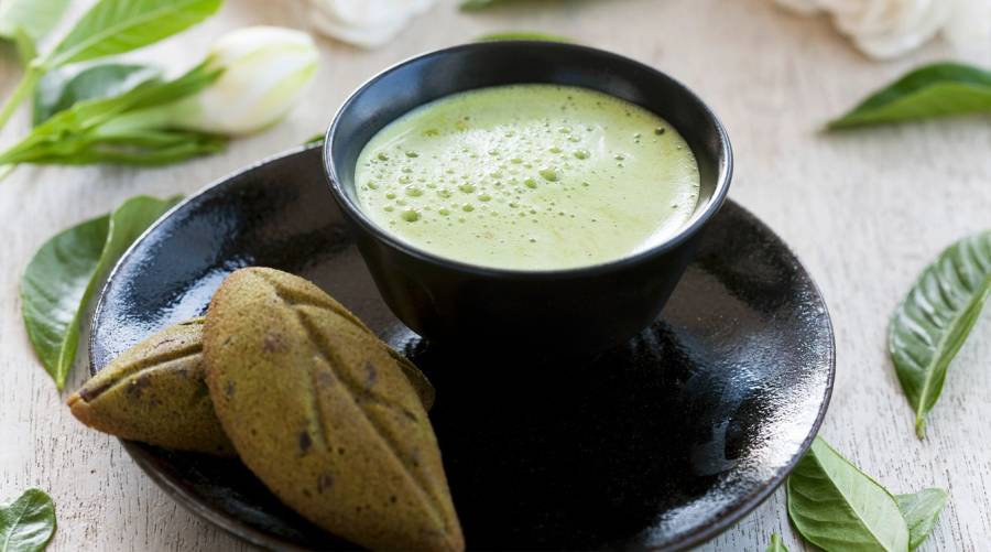 Matcha green tea powder in a bowl with a bamboo whisk on a wooden table