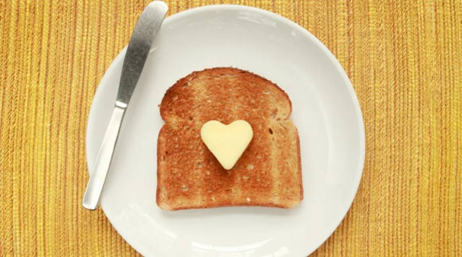 A colorful plate with sliced cheddar, crumbled feta, and Parmesan next to fruits and whole-grain crackers, promoting heart-healthy cheese eating.