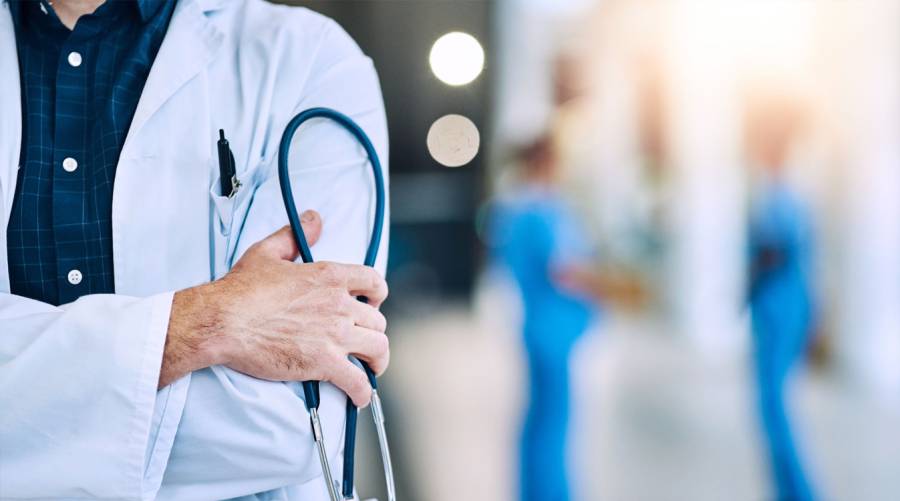 A close-up image of a doctor in a hospital setting with his hands tied, holding a stethoscope.
