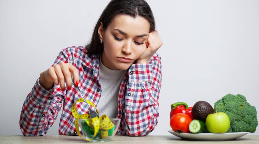 Depressed woman pushing vegetables with a fork, symbolizing the emotional impact of restrictive dieting