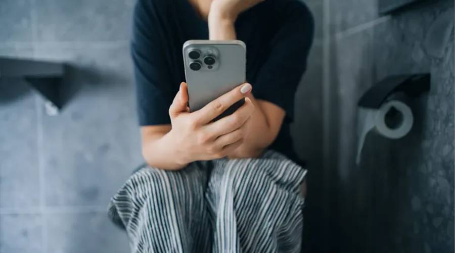 Person using smartphone on toilet — study links prolonged sitting to higher hemorrhoid risk.