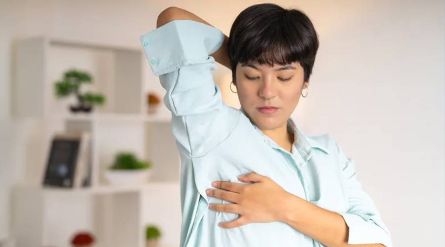 Woman performing breast self-awareness check in mirror for early breast cancer detection.