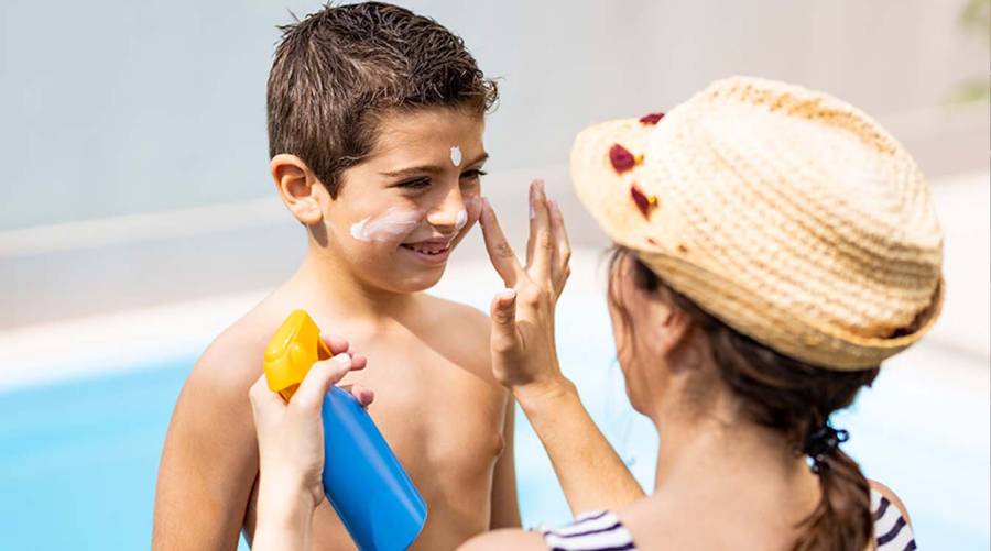 Person applying sunscreen on arms and face at the beach, affordable sunscreen bottle visible, sunny background