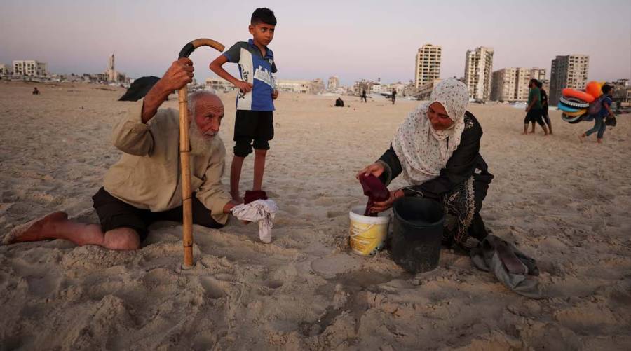 A displaced Palestinian woman washes clothes on the Mediterranean shore in Gaza City as severe water shortages and damaged infrastructure worsen the humanitarian and public health crisis.